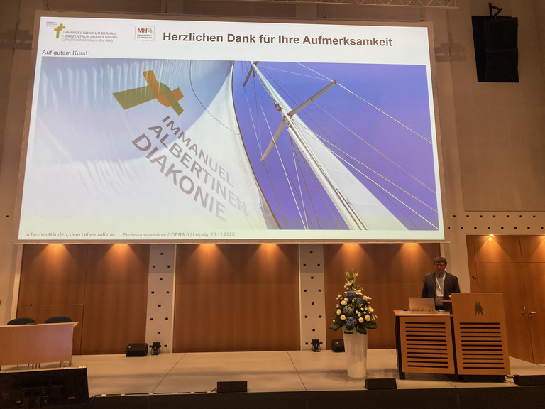 Der Leiter der Perfusiologie am Immanuel Klinikum Bernau Herzzentrum Brandenburg Torsten Müller stellt den Perfusionscontainer am Rednerpult auf der Bühne mit einer Leinwand bei der Internationalen Jahrestagung der Deutschen Gesellschaft für Perfusionsmedizin und der Fokustagung Herz der Deutschen Gesellschaft für Thorax-, Herz- und Gefäßchirurgie in Leipzig vor Der Leiter der Perfusiologie am Immanuel Klinikum Bernau Herzzentrum Brandenburg Torsten Müller stellt den Perfusionscontainer am Rednerpult auf der Bühne mit einer Leinwand bei der Internationalen Jahrestagung der Deutschen Gesellschaft für Perfusionsmedizin und der Fokustagung Herz der Deutschen Gesellschaft für Thorax-, Herz- und Gefäßchirurgie in Leipzig vor