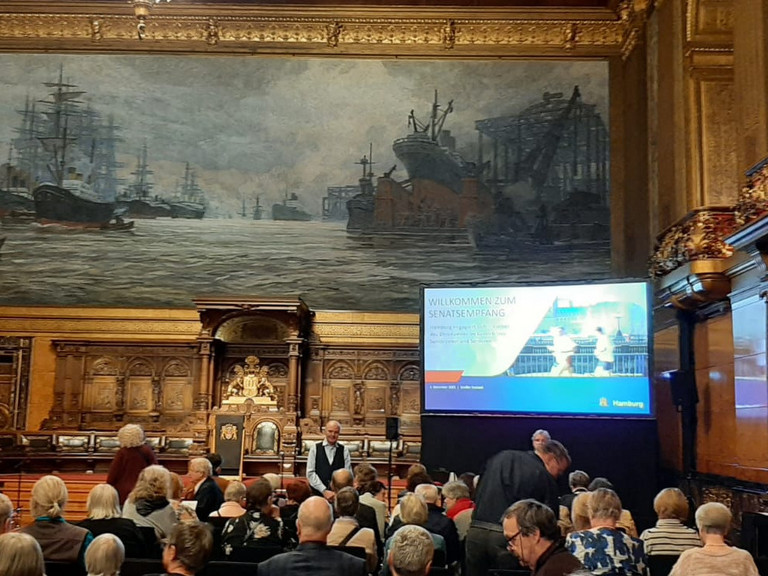 Blick über die Stuhlreihen mit Publikum im Festsaal des Hamburger Rathauses Richtung Podium mit einem großen Monitor zum Senatsempfang für ehrenamtlich engagierte Menschen mit Ehrung der Ehrenamtlichen im Albertinen Haus Hamburg Blick über die Stuhlreihen mit Publikum im Festsaal des Hamburger Rathauses Richtung Podium mit einem großen Monitor zum Senatsempfang für ehrenamtlich engagierte Menschen mit Ehrung der Ehrenamtlichen im Albertinen Haus Hamburg