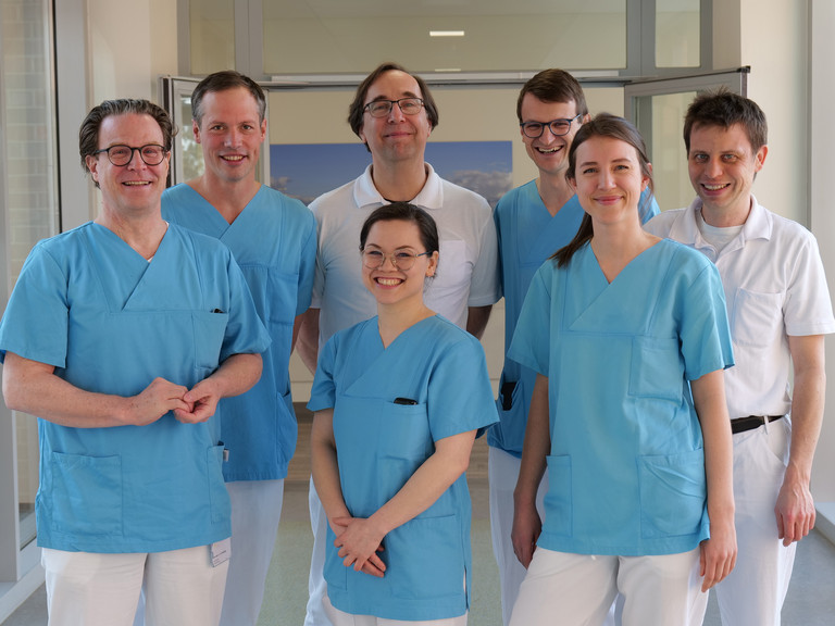 Das Team Des Mitralklappen-Zentrums des Albertinen Herz- und Gefäßzentrums am Standort Hamburg Schnelsen lächelt auf einem Flur in Arztkleidung in die Kamera Das Team Des Mitralklappen-Zentrums des Albertinen Herz- und Gefäßzentrums am Standort Hamburg Schnelsen lächelt auf einem Flur in Arztkleidung in die Kamera