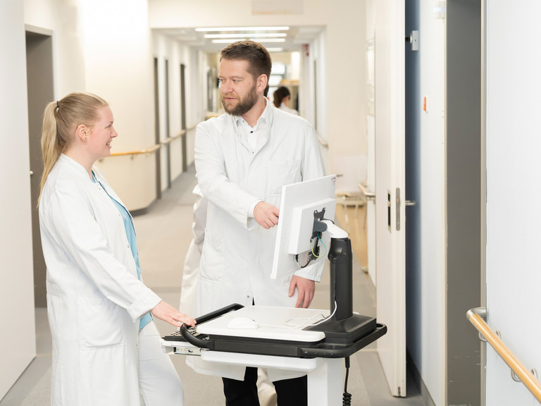 Prof. Dr. med. Torsten Diekhoff spricht mit einer Medizinstudentin an einem mobilen Visitenwagen auf dem Flur - Immanuel Klinik Rüdersdorf - Nachricht - Weiterbildungsbefugnisse stärken ärztlichen Nachwuchs in Rüdersdorf Prof. Dr. med. Torsten Diekhoff spricht mit einer Medizinstudentin an einem mobilen Visitenwagen auf dem Flur - Immanuel Klinik Rüdersdorf - Nachricht - Weiterbildungsbefugnisse stärken ärztlichen Nachwuchs in Rüdersdorf