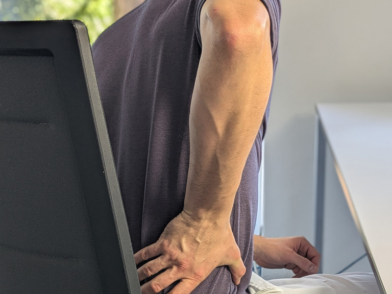 Mann sitzt auf Stuhl und hält Hand an unteren Rücken Mann sitzt auf Stuhl und hält Hand an unteren Rücken
