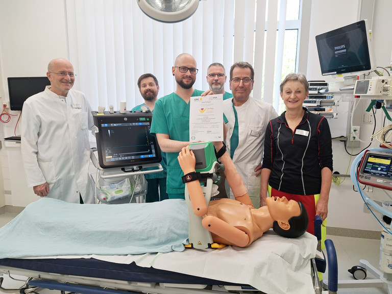 Im Schockraum der Zentralen Notaufnahme im Immanuel Klinikum Bernau Herzzentrum Brandenburg zeigen die Spezialistinnen und Spezialisten aus der Zentralen Notaufnahme, der Intensivmedizin und der Kardiologie des Immanuel Klinikum Bernau Herzzentrum Brandenburg stolz das Zertifikat „Cardiac Arrest Center“ Im Schockraum der Zentralen Notaufnahme im Immanuel Klinikum Bernau Herzzentrum Brandenburg zeigen die Spezialistinnen und Spezialisten aus der Zentralen Notaufnahme, der Intensivmedizin und der Kardiologie des Immanuel Klinikum Bernau Herzzentrum Brandenburg stolz das Zertifikat „Cardiac Arrest Center“