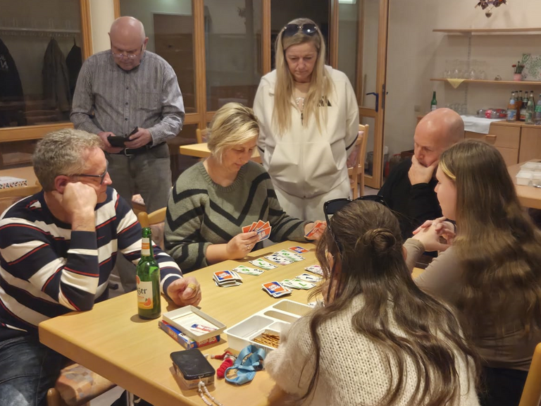 Mehrere Teammitglieder sitzen und stehen an einem Tisch beim Kartenspielen in der Immanuel Begegnungsstätte Ecktannen im Heilbad Waren beim gemeinsamen Spieleabend für Mitarbeitende der Seniorenpflegeeinrichtung mit Tagespflegeangebot Immanuel Haus Ecktannen. Mehrere Teammitglieder sitzen und stehen an einem Tisch beim Kartenspielen in der Immanuel Begegnungsstätte Ecktannen im Heilbad Waren beim gemeinsamen Spieleabend für Mitarbeitende der Seniorenpflegeeinrichtung mit Tagespflegeangebot Immanuel Haus Ecktannen.