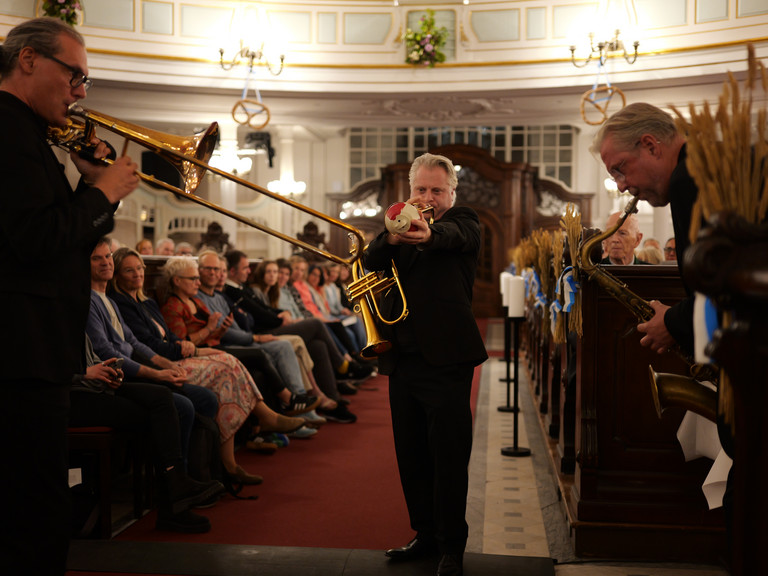 Ein Blechbläser läuft musizierend und in Begleitung von zwei anderen Bläsern des Trios "Windspiel" der NDR Bigband durch die mit Publikum besetzten Kirchengänge beim 10. Herzbrücke-Benefizkonzert im Hamburger „Michel“ der Albertinen-Stiftung. Ein Blechbläser läuft musizierend und in Begleitung von zwei anderen Bläsern des Trios "Windspiel" der NDR Bigband durch die mit Publikum besetzten Kirchengänge beim 10. Herzbrücke-Benefizkonzert im Hamburger „Michel“ der Albertinen-Stiftung.
